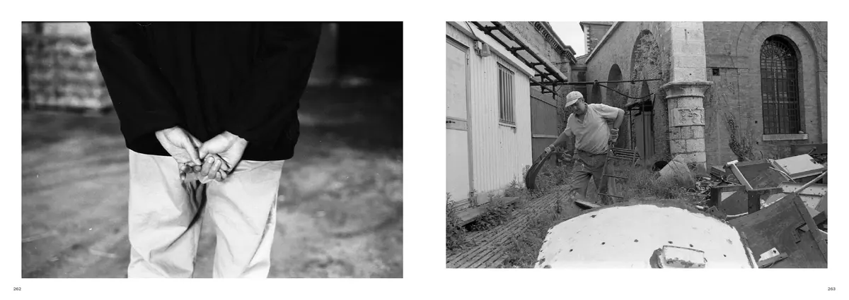 Hands clasped behind a sculptor's back, facing a courtyard of brick and timber