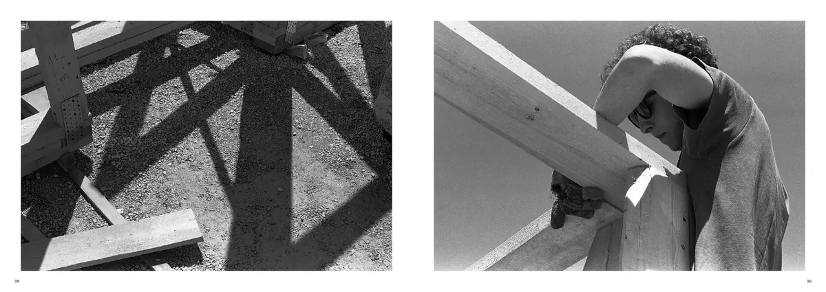 Shadows of the timber frame on gravel, facing a builder with a beam on his shoulder