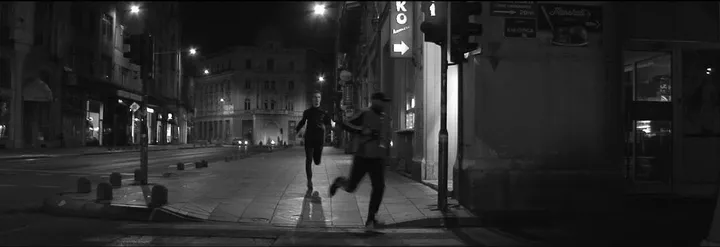 Two men run down an empty street at night, under the streetlights