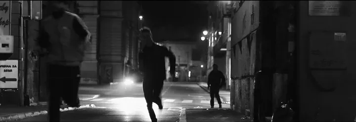 Runners in a narrow street, a car's headlights behind them
