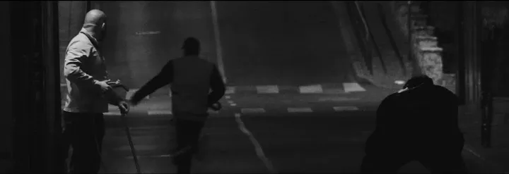 Three men in a dark street: one with a stick, one running, one bent over
