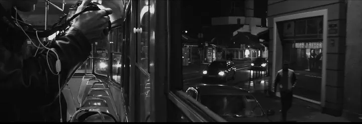 A hand on a tram rail, the night street seen through the window, a man running outside